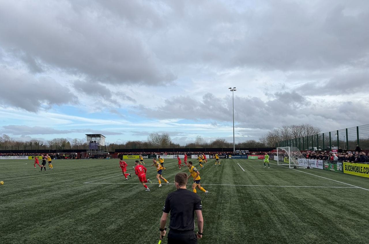 A match in progress at the Elmbridge Xcel Sports Hub, seen from the touchline under a cloudy sky