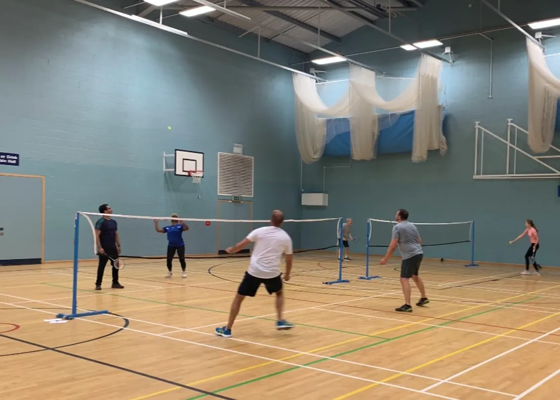 Players spread across two badminton courts in a sports hall, with games in progress at both nets