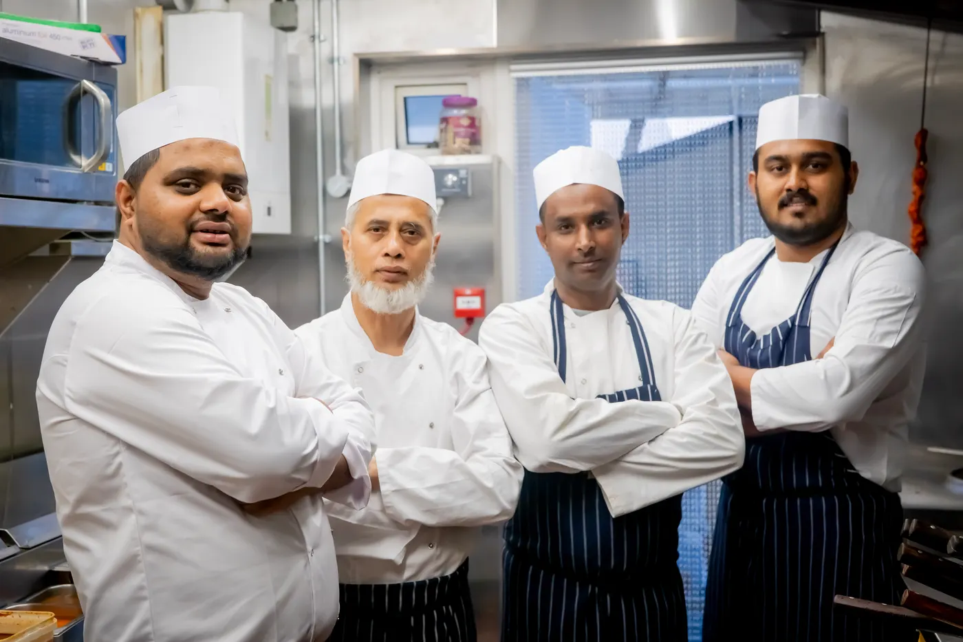 Four Khyber Pass chefs in whites and striped aprons in the restaurant's kitchen