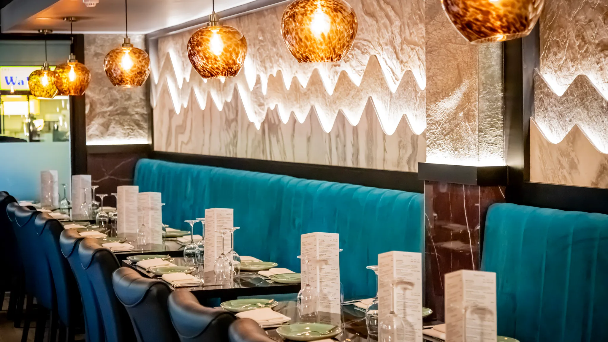 Laid tables running the length of the Khyber Pass dining room, beneath a row of copper glass pendant lights and beside a teal velvet banquette