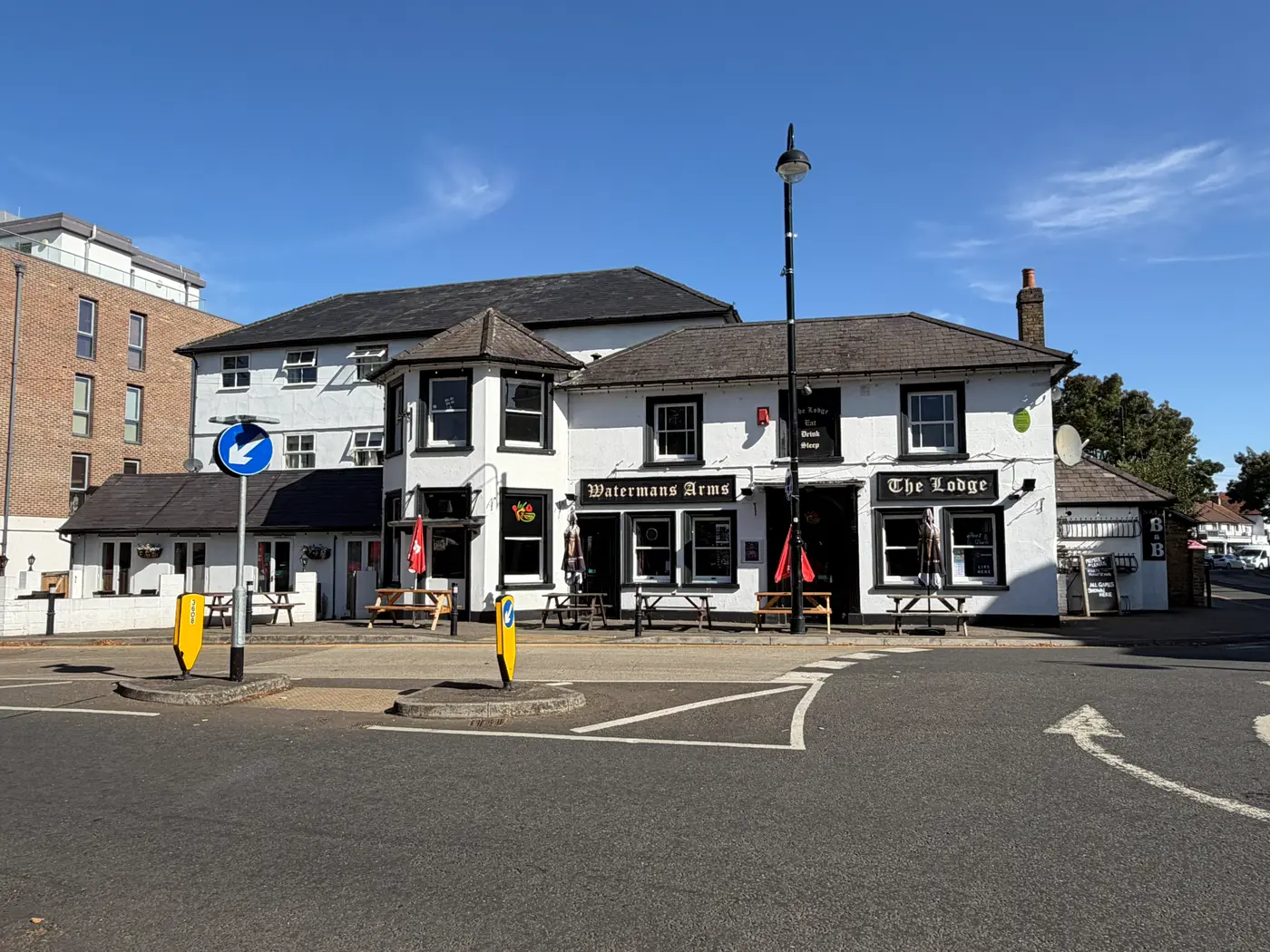 The Watermans Arms seen across the road junction, a two-storey white pub on the corner with a modern brick apartment block beyond it