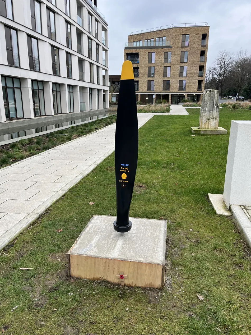 A propeller blade memorial sculpture at Walton Court Gardens, with a wooden poppy cross at its base