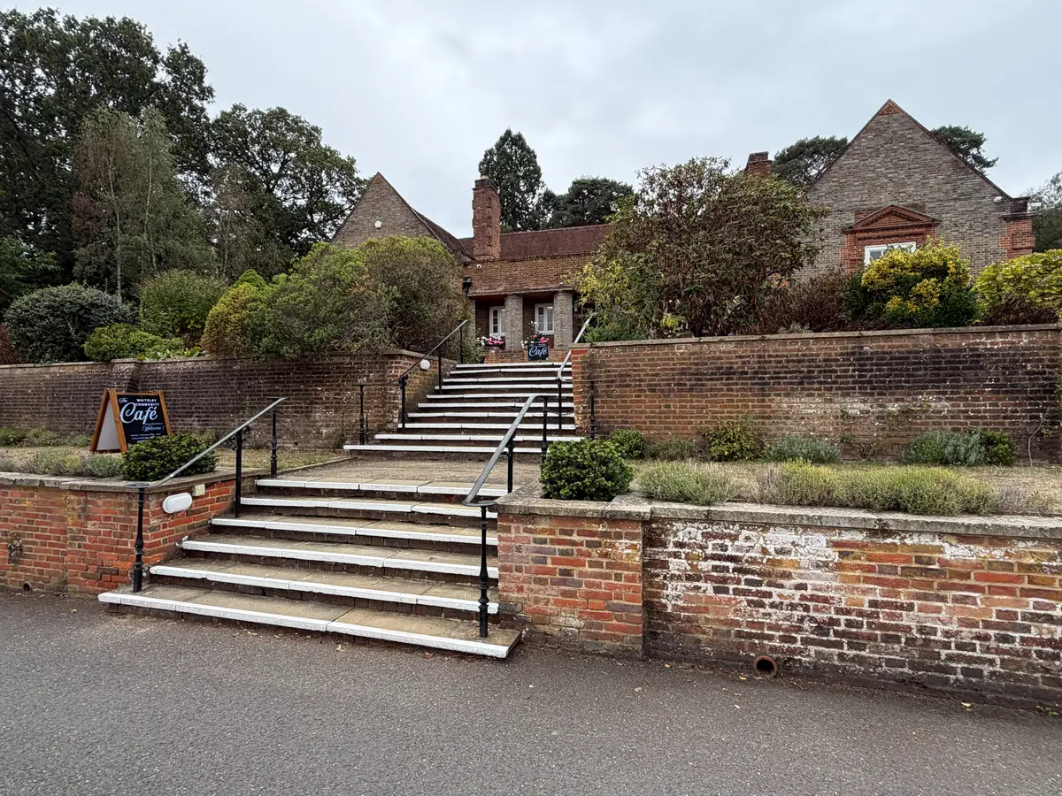 Wide steps with metal handrails climbing between brick retaining walls to a brick building, with a café A-board on the left