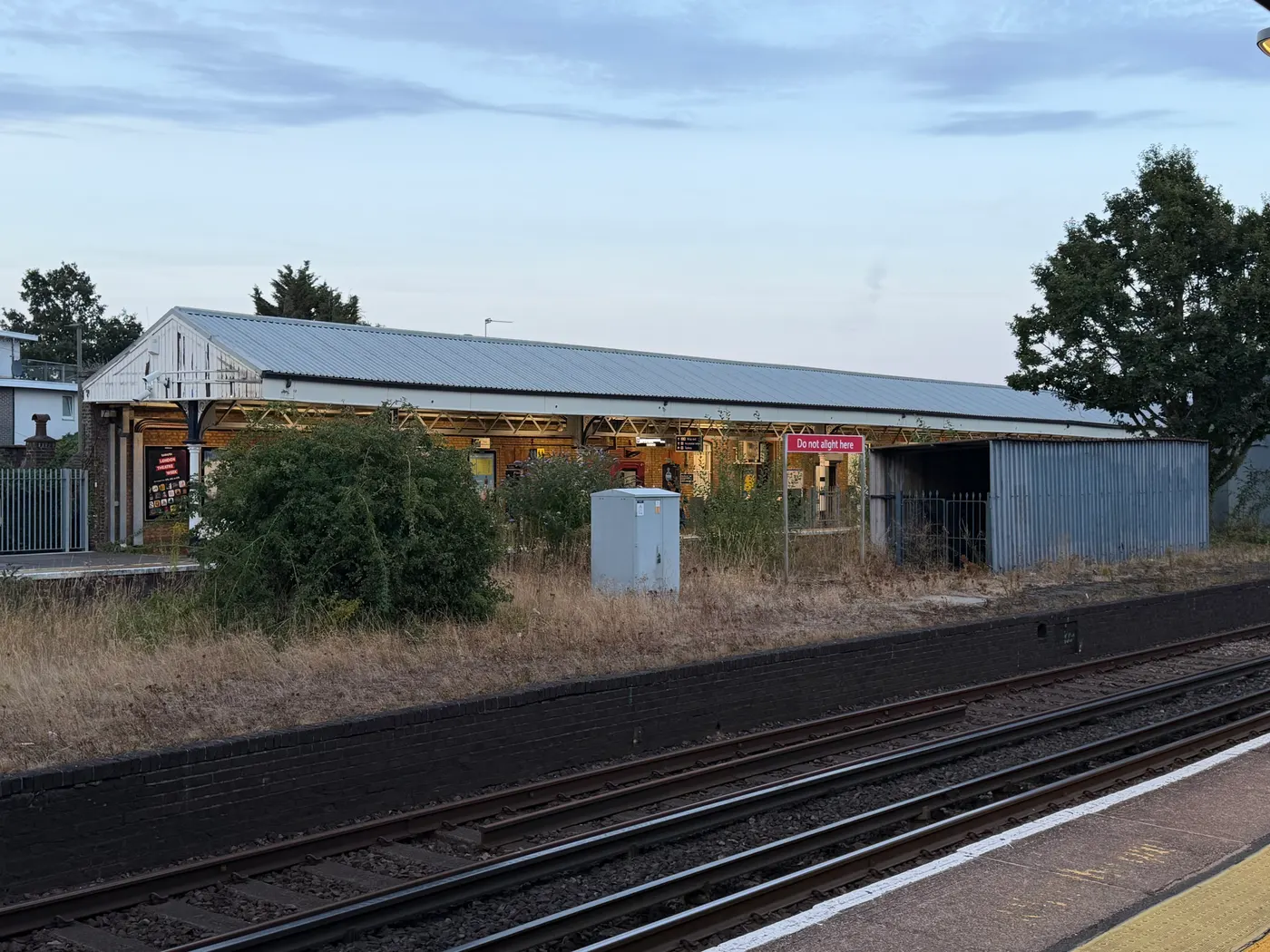 Platform 1 at Walton-on-Thames seen from Platform 2 across the tracks, its long canopied building set behind the brick face of a disused centre platform carrying a red Do not alight here sign