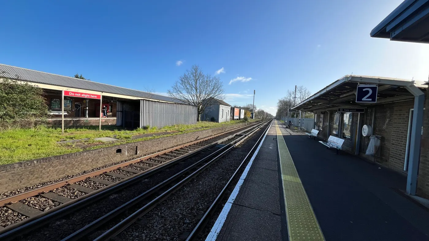 Platform 2 at Walton-on-Thames station, with its canopy, seating and blue number 2 sign on the right, and the long canopied building on the Platform 1 side across the tracks