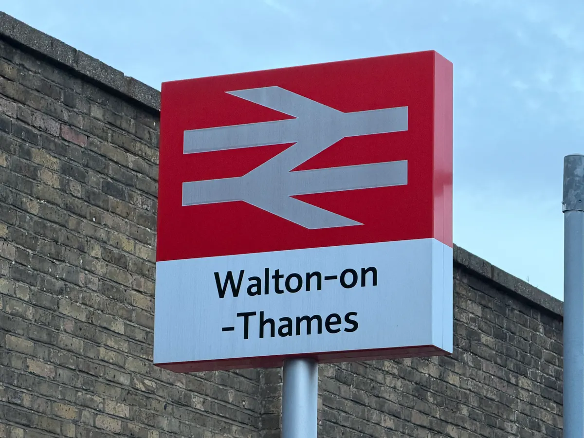 The National Rail double arrow totem sign reading Walton-on-Thames, mounted on a post in front of the station's brick boundary wall